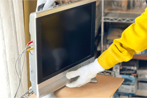 古いテレビを運ぶ作業着姿の人